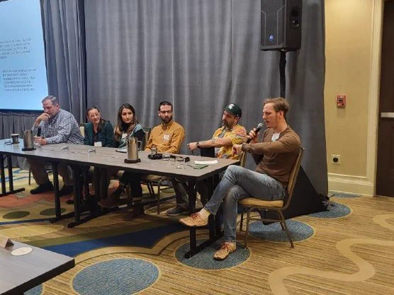 Six people sitting at the table, being part of the panel to discuss with each other. One person is currently talking with the microphone.