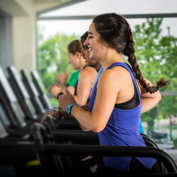 Three individuals running on treadmills in a gym, focusing intently on their workout.