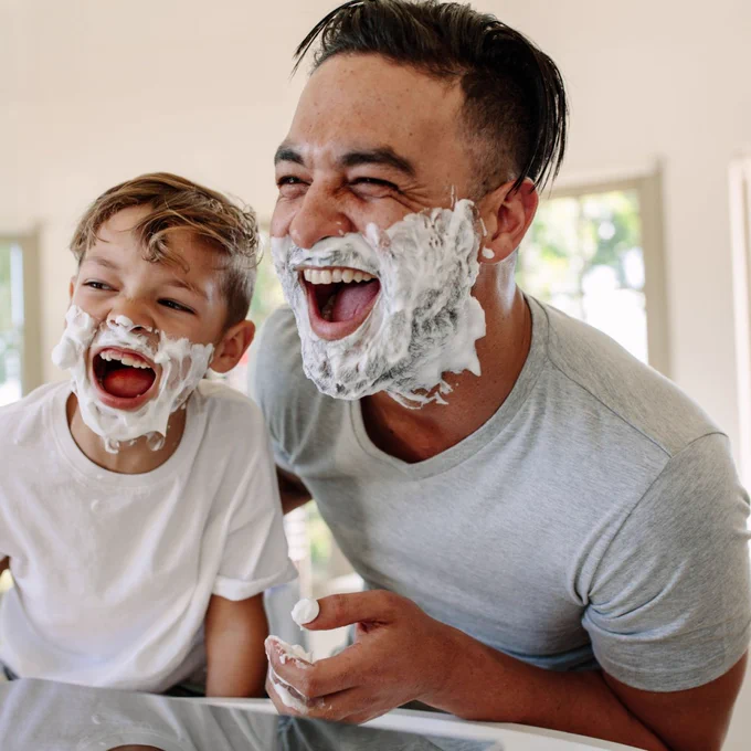 Dad and young son laugh with shaving cream on their faces