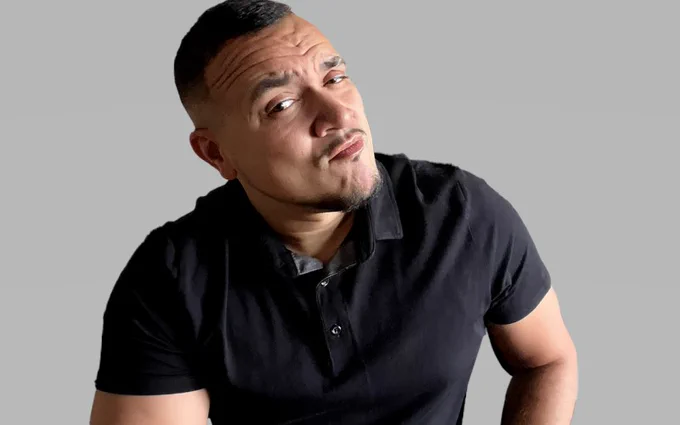 Person with a quizzical expression wearing a black polo shirt against a grey background.