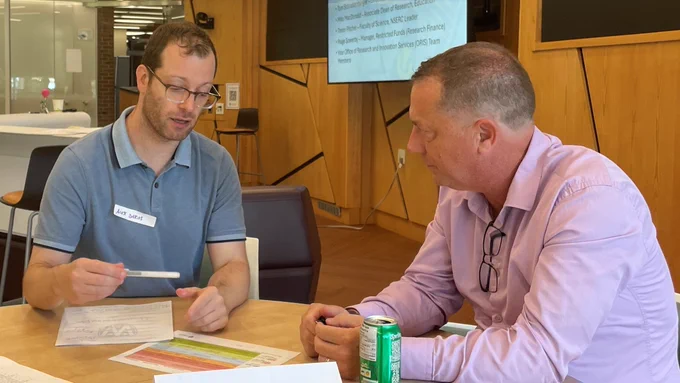 Two people sitting at a table writing on a document. 