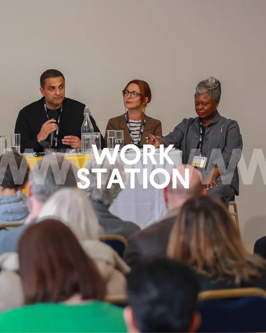 Three panelists sit at a table during a conference at an event titled "WORK STATION". The audience is visible in the foreground listening attentively.