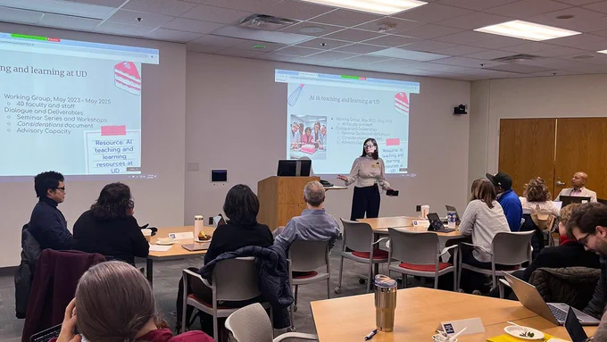 Librarian stands beside a podium and speaks to a room of faculty members at the University of Delaware.