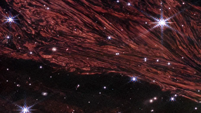 These shimmering cosmic curtains show interstellar gas and dust that has been heated by the flashbulb explosion of a long-ago supernova. The gas then glows infrared light in what is known as a thermal light echo. As the supernova illumination travels through space at the speed of light, the echo appears to expand. NASA’s James Webb Space Telescope observed this light echo in the vicinity of the supernova remnant Cassiopeia A. NASA, ESA, CSA, STScI, J. Jencson (Caltech/IPAC)