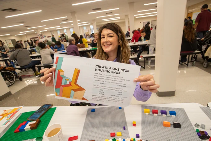 A person holding up a paper that says "Create a One-Stop Housing Shop" at a table with legos.