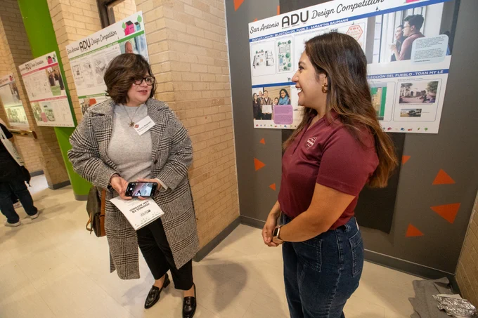 Two people speaking to each other in front of a project board.