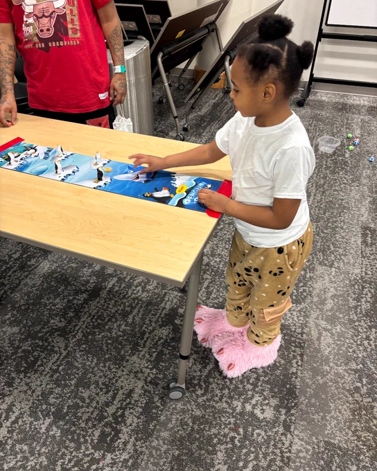 A child in a white shirt and patterned pants playing with LEGO toys on a table.