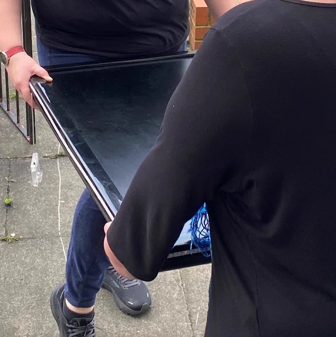 Photo shows two people carrying a flatscreen TV between them. 
