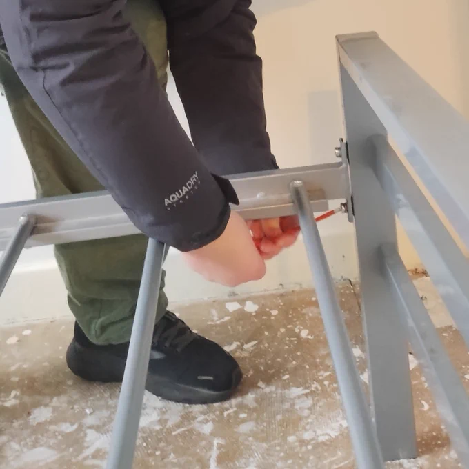 Photo shows hands holding an allen key to fit together a silver bed frame. 