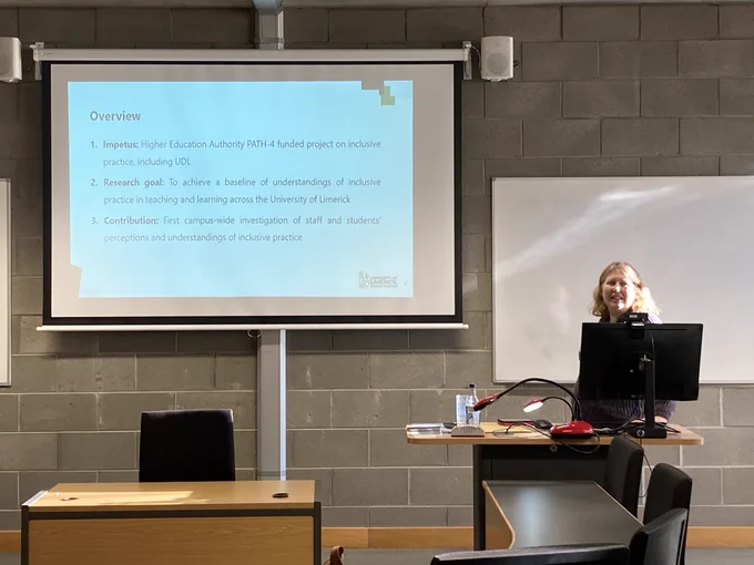 Sadhbh O’Dwyer standing to the right of a presentation screen, which shows an overview of her presentation.