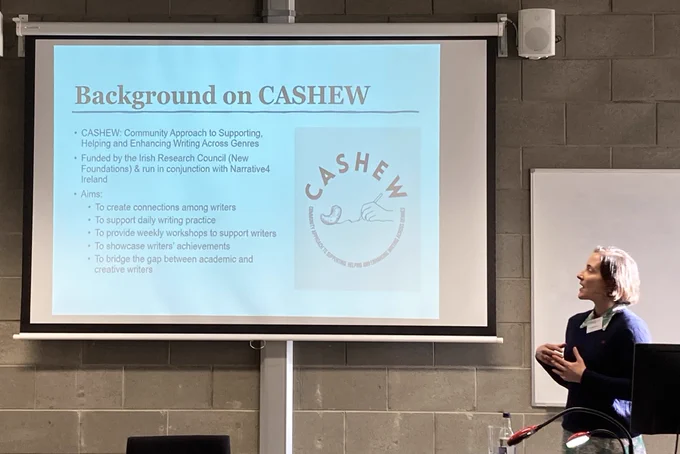 Christina (Tina) Morin standing to the right of a screen, which shows a slide on the background on the CASHEW project.