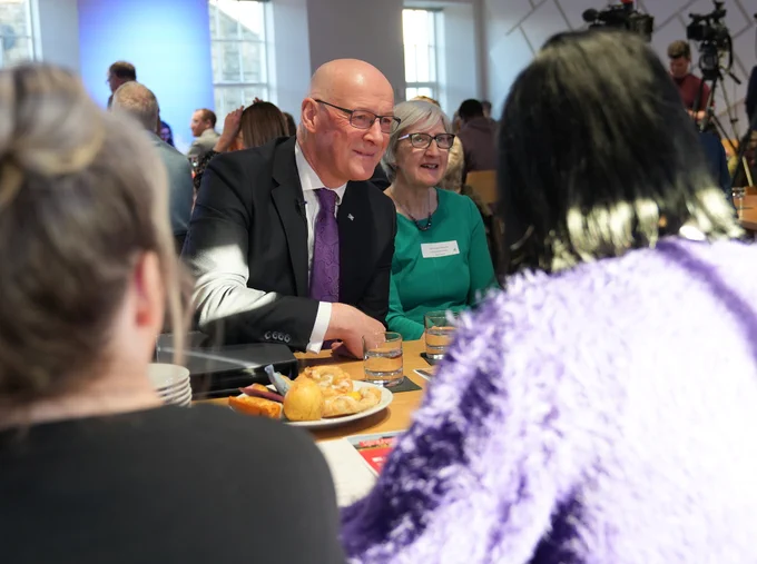 First Minister John Swinney sits at a table with attendees at the Robertson Trust event in Stirling.