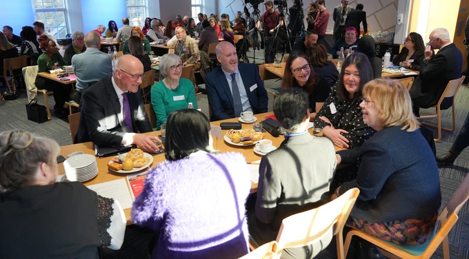 First Minister John Swinney sits at a table with attendees at the Robertson Trust event in Stirling.