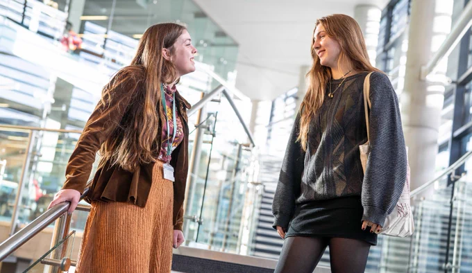 Member of staff and student standing in the Bill Bryson Library, smiling and talking.