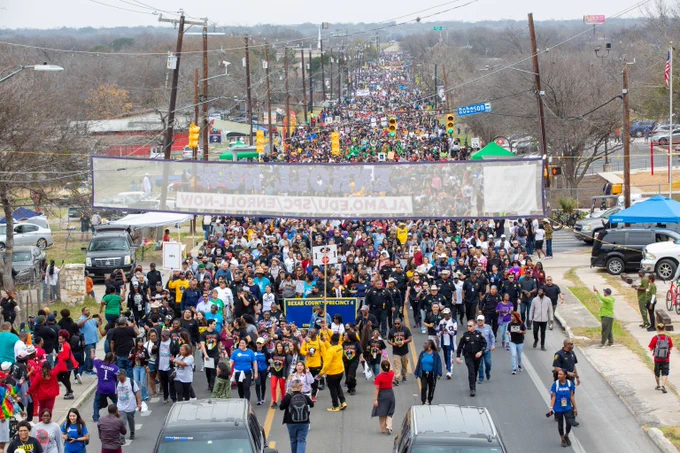 An aerial view of a large gathering of people marching in the street.