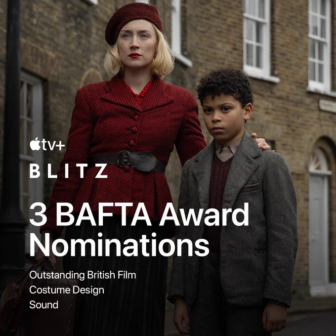 From Blitz. Wearing a red hat and a red jacket, Saoirse Ronan as Rita has her arm around Elliott Heffernan as George, who is wearing a sweater underneath a gray jacket. Both are looking ahead calmly while wearing serious expressions on their faces.