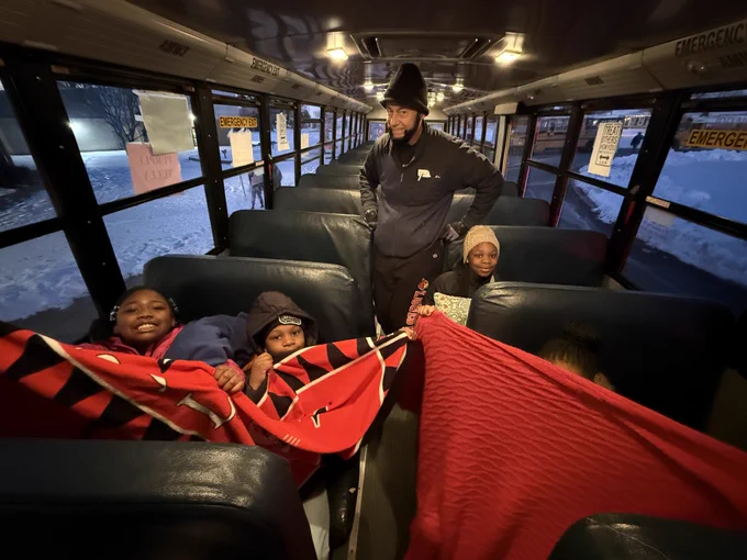 Four students pose for a picture on a school bus holding blankets while a bus driver stands in the background.