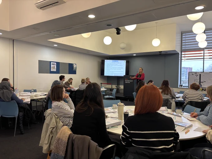 A Destination Reader team member stands in front of a room full of people giving a presentation next to a screen