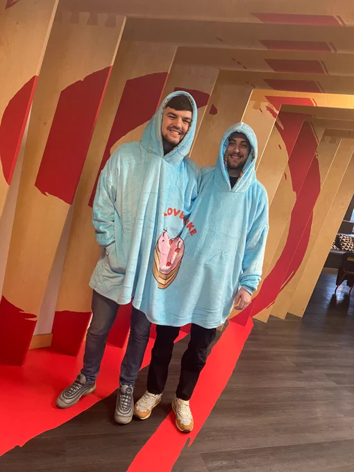 Two people wear a conjoined pyjama hoodie.