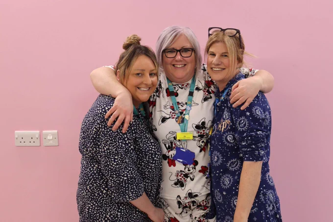 Three women wearing pyjamas smile and embrace. 