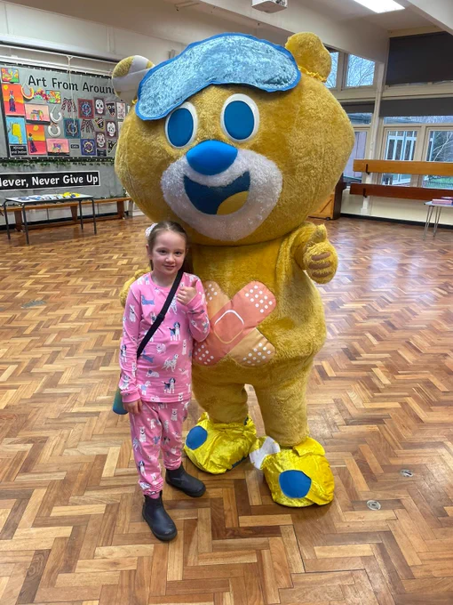 A little girl wearing pyjamas poses with a yellow bear mascot.