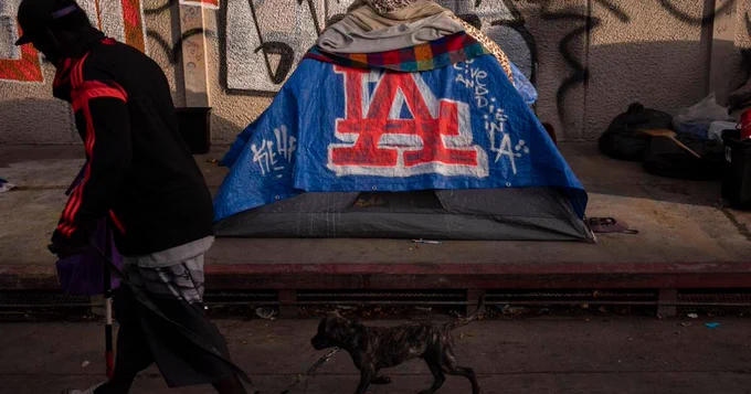 a person walks their dog past a tent covered by a blankets with the LA (los angelos) logo