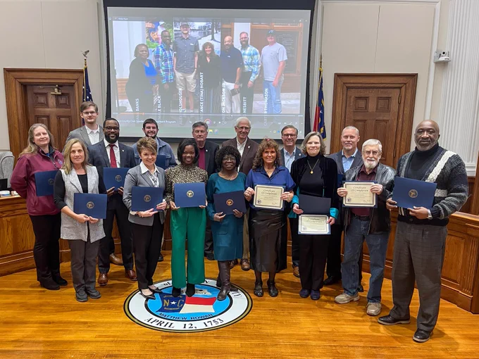 Group of 13 citizens post holding certificates in Board of Commissioners chambers.