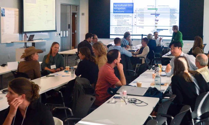 Group of people attending a workshop in a conference room with presentation slides related to Agricultural GHG Mitigation Solutions.
