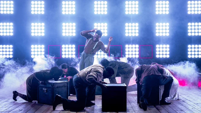 Romario Simpson, surrounded by the rest of the cast, in The Lonely Londoners