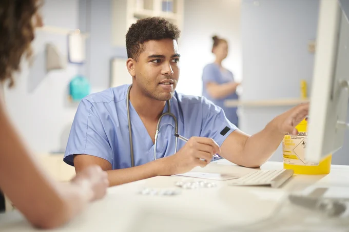 A clinician wearing scrubs looks at notes on a computer screen
