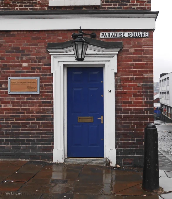 An elegant blue door in a Georgian doorcase, with a lamp hanging above. A sign reads 'Paradise Square' above it and too the right.