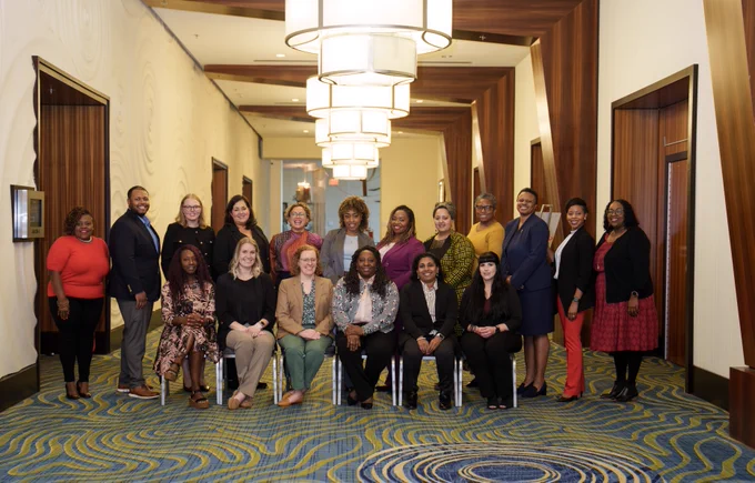 Group of diverse professionals posing for a photo in a hotel hallway with an elegant carpet and modern light fixtures.
