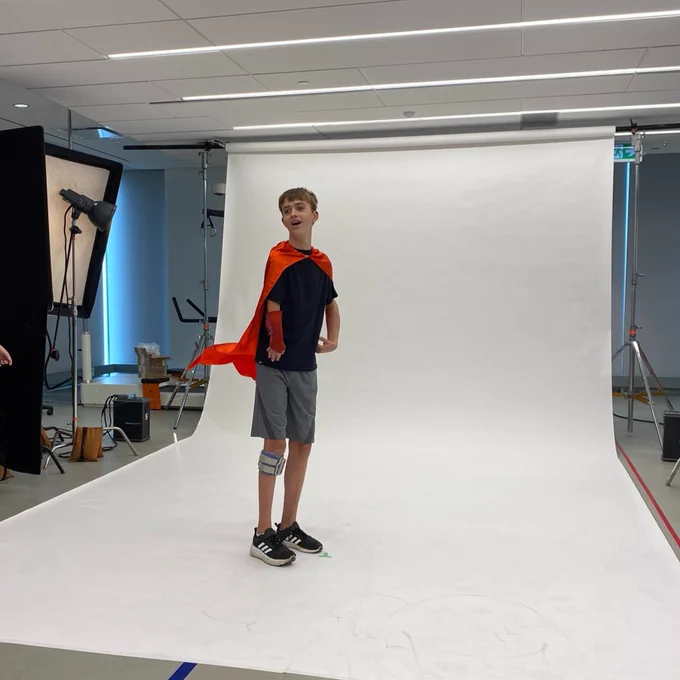 A teen wearing a red cape in a photography studio with a white backdrop