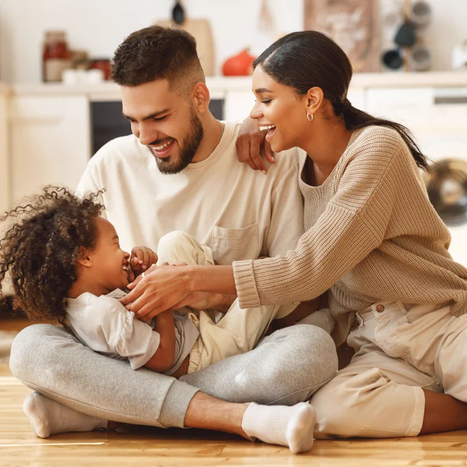 Mom, dad, and daughter play and laugh together on the floor of their home