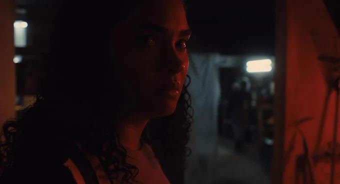 A young dark haired woman looks tensely towards us bathed in red light. Brittany O'Grady in Pedro Kos’ debut feature IN OUR BLOOD.