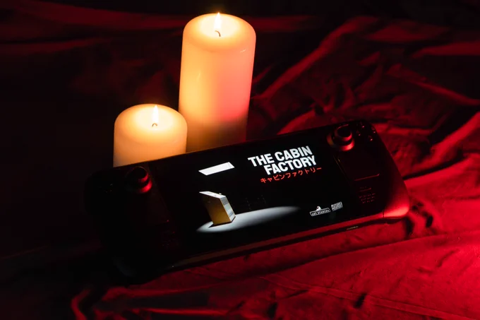 Photograph of a Steam Deck with The Cabin Factory running on it. There's red mood lighting and candles in the backdrop.