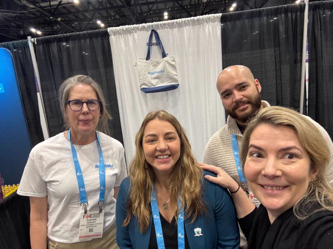 Four individuals smiling at a trade show booth with a banner reading "ReadWorks" in the background.