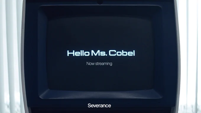 A black television, with the word "Severance" on the bottom, sits in the middle of window blinds. The screen displays the words, "Hello Ms. Cobel" and "Now Streaming."