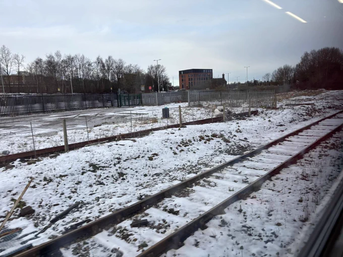 The view of a snowy field out of the window of a train. Chunky snow with the mountains in the background