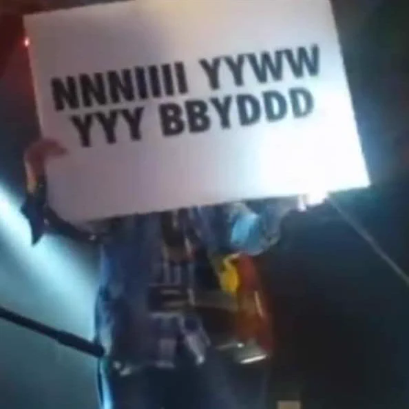 Gruff Rhys holding a "Ni Yw Y Byd" sign, styled "NNNIIII YYWW YYY BBYDDD" (live at Hanner Cant, 2012)