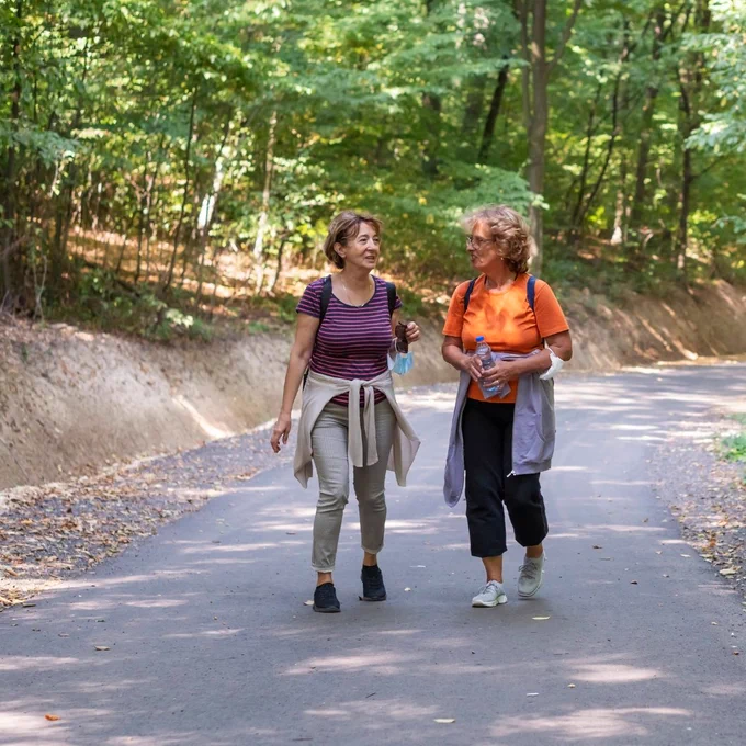 Two women walking through a forest whilst chatting to each other.