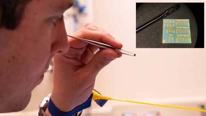 tiny space chip held in tweezers and compared to a needle