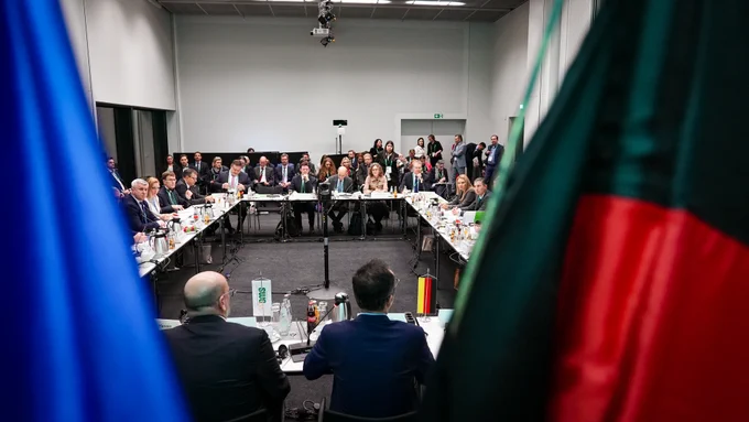 Blick in den Sitzungssaal - im Vordergrund unscharf die Flaggen der EU und Deutschlands.
