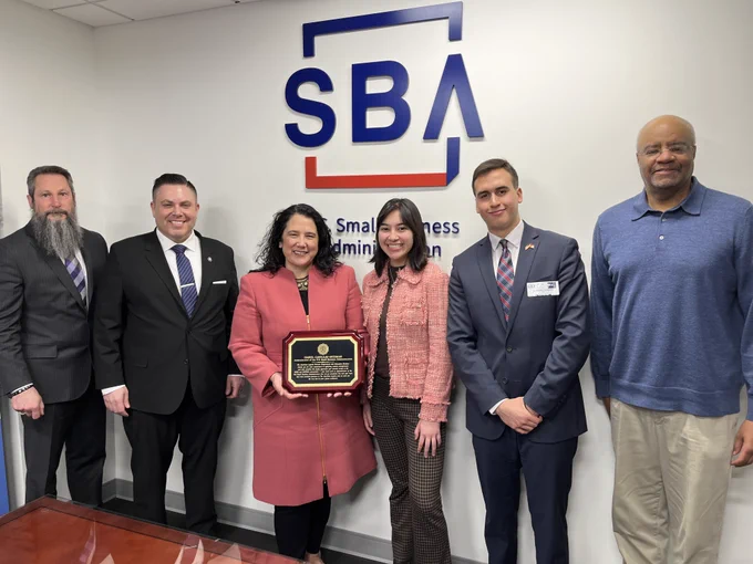 Group of six individuals posing with an award in front of the Small Business Administration logo.