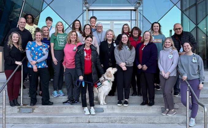 Group of people and a service dog posing on steps outside a modern building, expressing camaraderie.