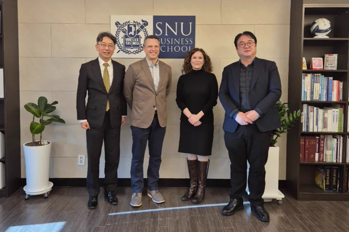 Four individuals standing and smiling in front of a banner with the Seoul National University Business School logo. 