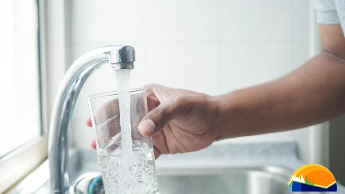 A person filling a clear glass with water from a kitchen tap.