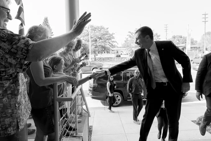 Black-and-white image of Secretary Pete Buttigieg shaking hands with a child at an event. 