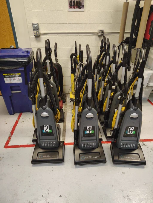 A row of numbered commercial vacuum cleaners lined up in a storage area.