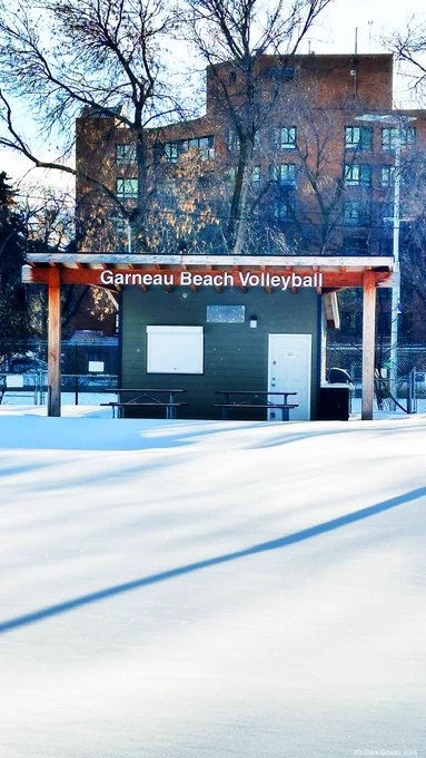 Snowy foreground, Garneau Beach Volleyball sign and hug in mid ground, high rise and trees in background
